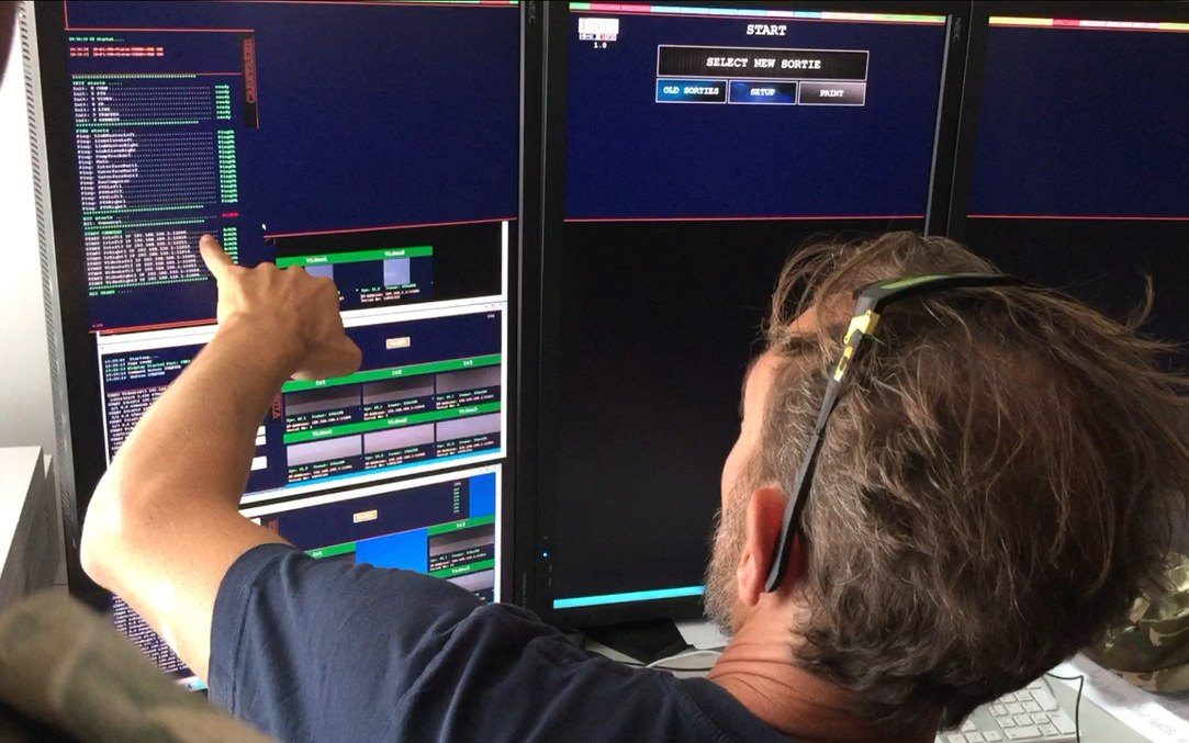Engineer at an operator console, pointing at a running sortie log